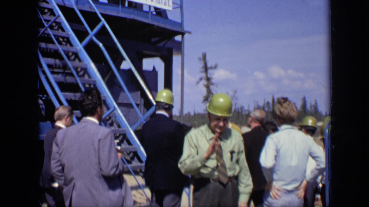 Men in suits and yellow hard hats stand near a blue metal stairway at an outdoor worksite.