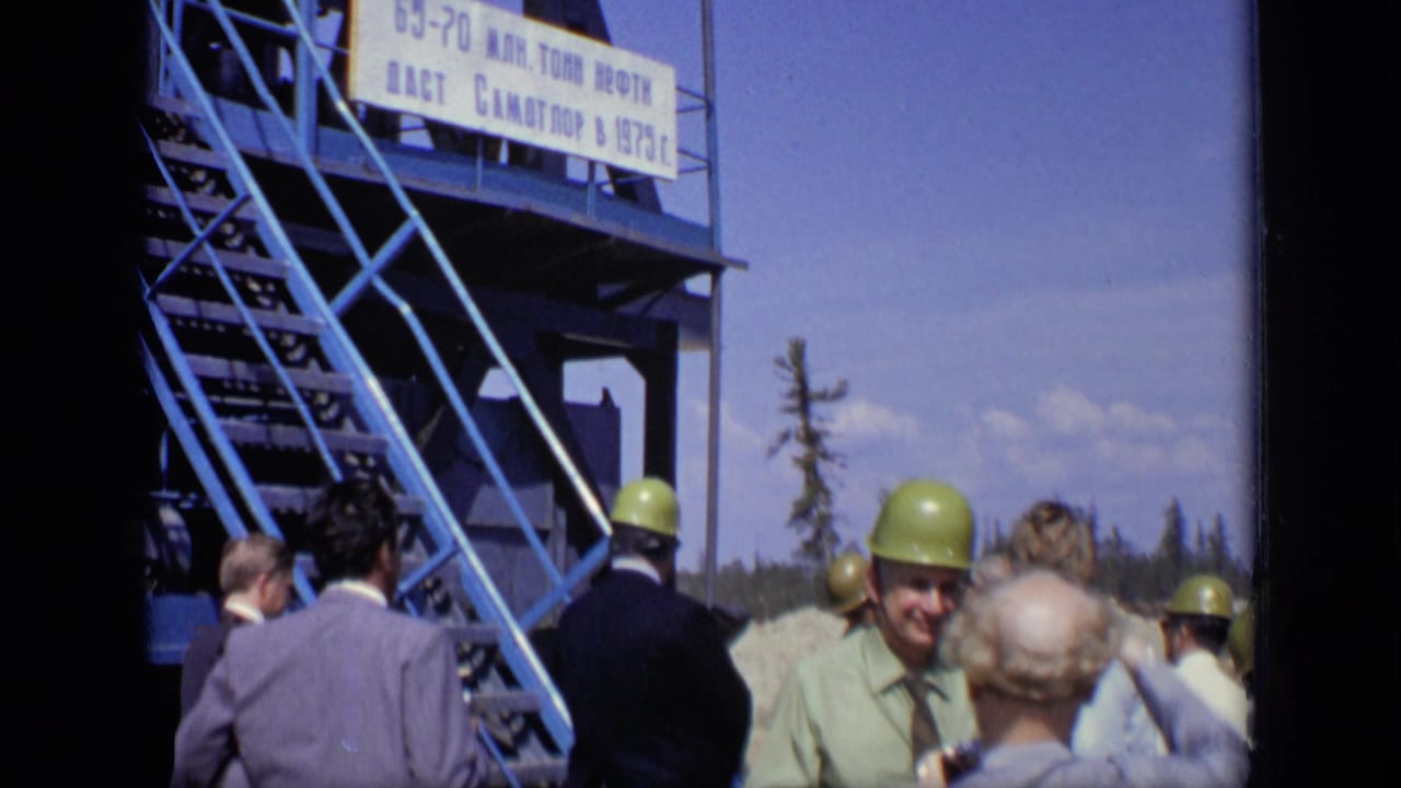 In 1971 Moscow footage, hard-hatted visitors stand at an industrial site below a blue staircase and large Cyrillic production sign.