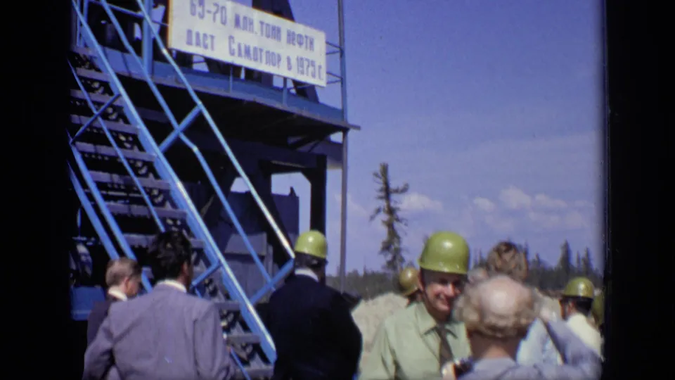In 1971 Moscow footage, hard-hatted visitors stand at an industrial site below a blue staircase and large Cyrillic production sign.