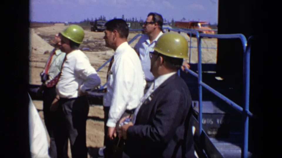 The 1971 Moscow scene shows hard-hatted visitors near blue railings, with industrial equipment and open ground behind them.