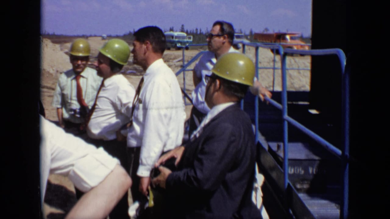 A group of men in hard hats and business clothes stand beside blue steps at a work site.