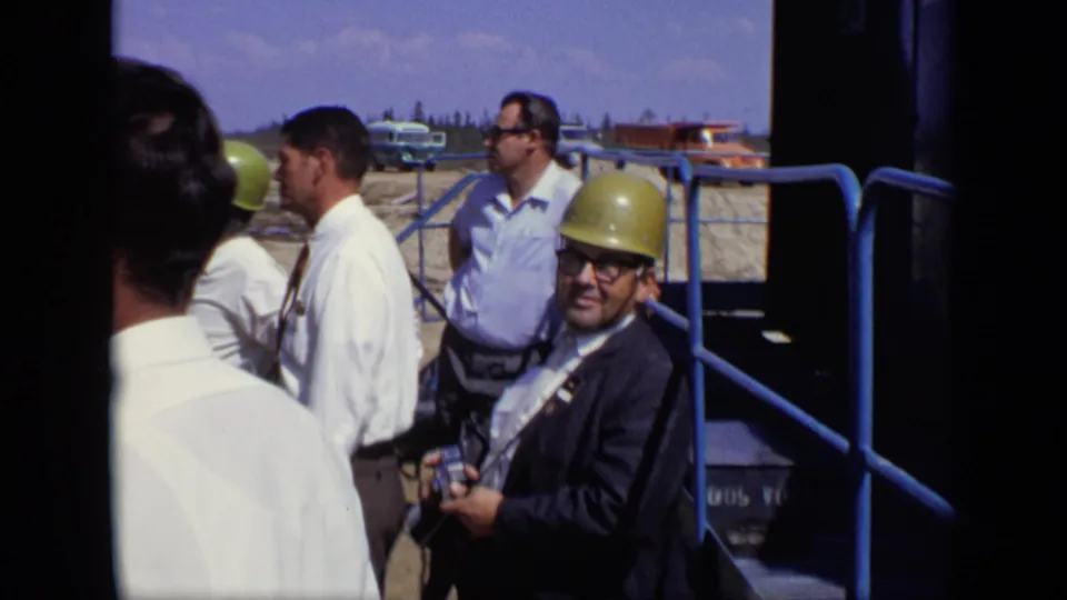 A suited man in a yellow hard hat smiles toward the camera during the supported 1971 Moscow construction-site visit.
