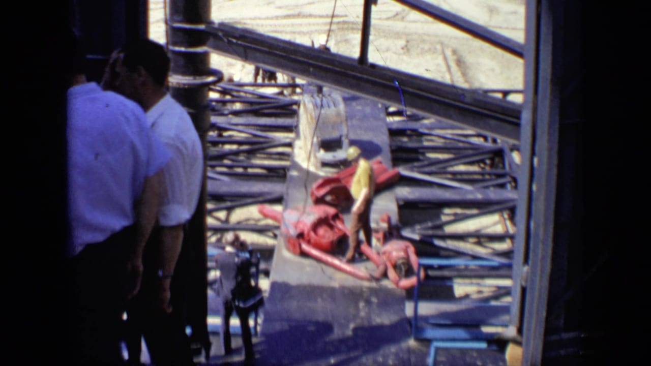Men in white shirts stand partly in shadow at a Moscow construction site, with steel beams, hoses, and red equipment beyond them.