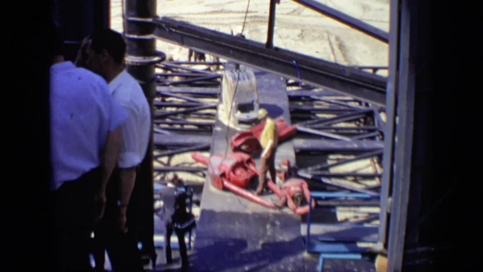 Men in white shirts stand partly in shadow at a Moscow construction site, with steel beams, hoses, and red equipment beyond them.