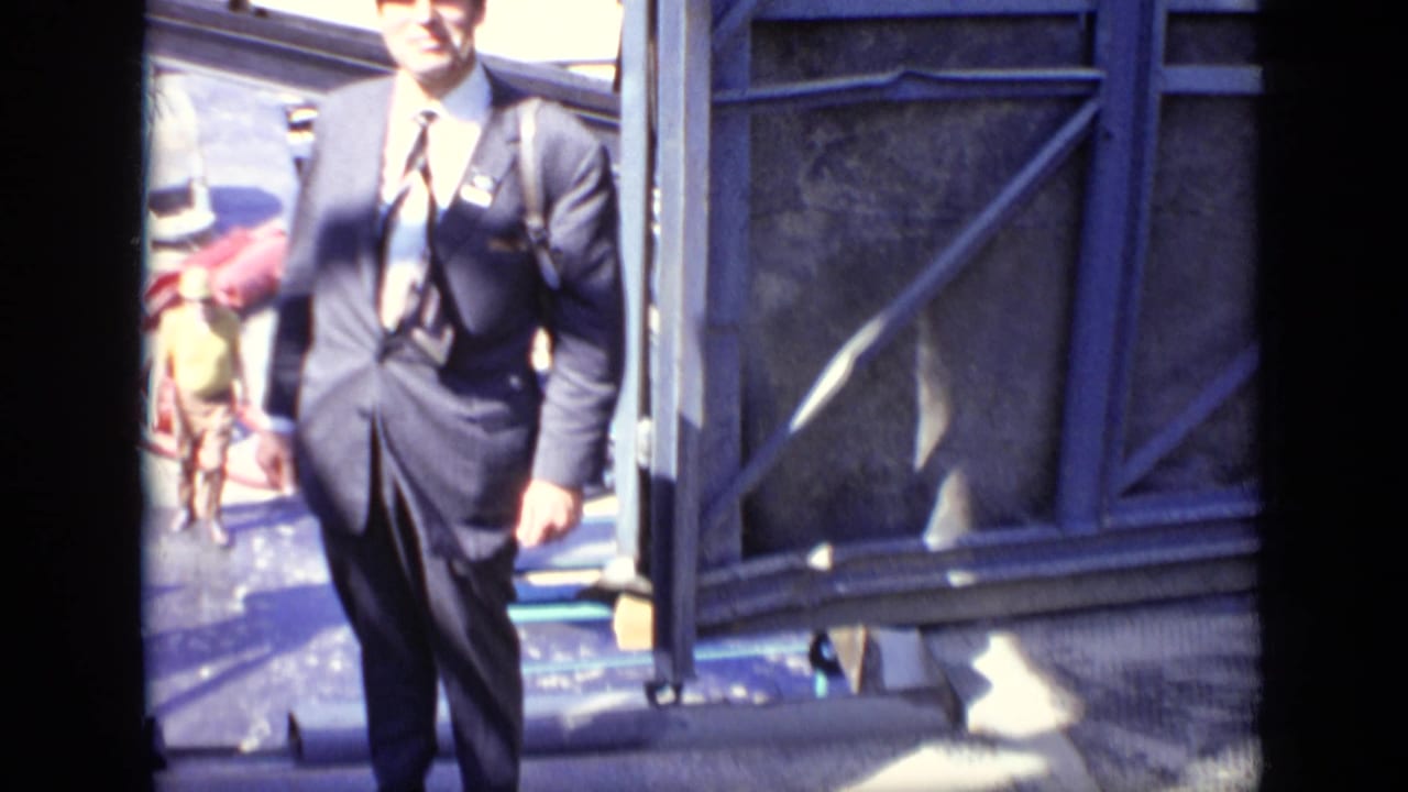 Suited man walks beside a construction structure with workers behind him.