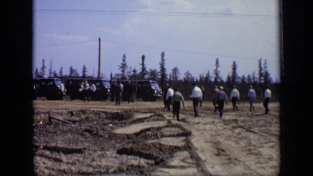 1971 Moscow 8mm frame showing men crossing rough ground toward dark vans beside a sparse pine tree line.