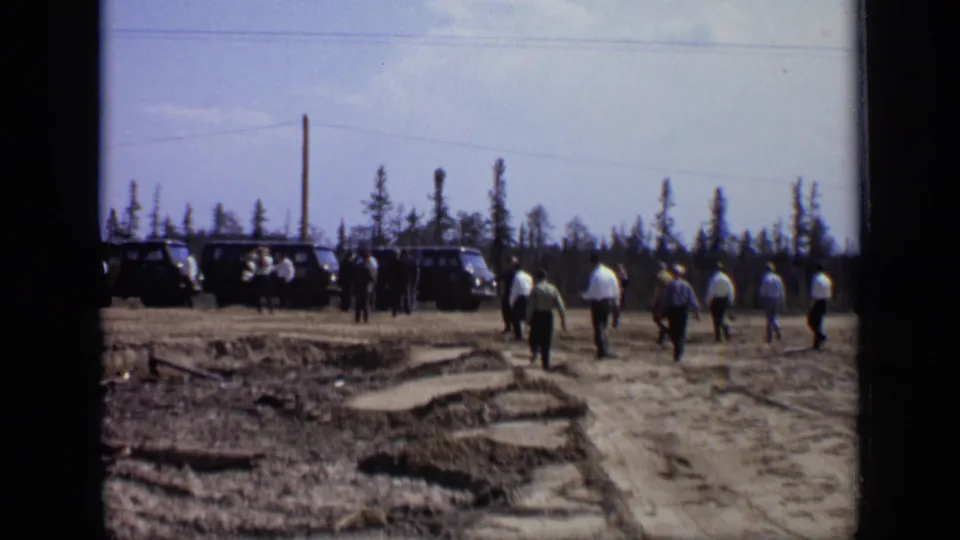 1971 Moscow 8mm frame showing men crossing rough ground toward dark vans beside a sparse pine tree line.
