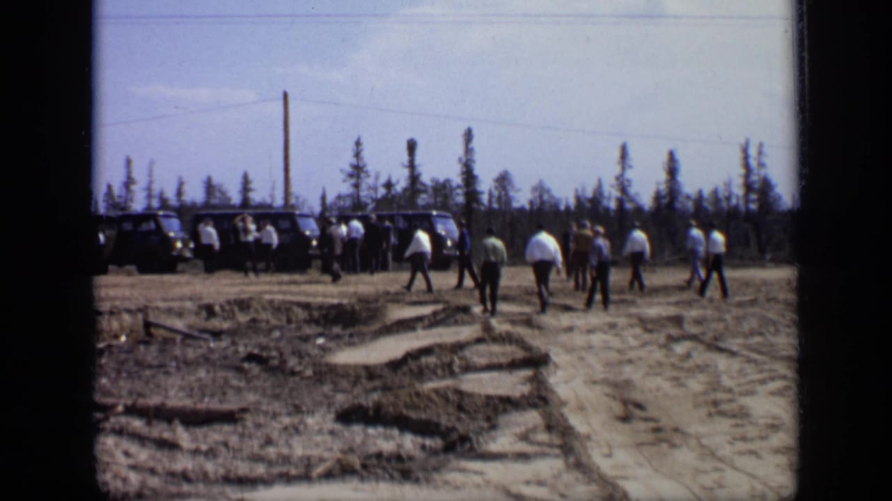 Men in suits and shirts continue toward parked vans at an outdoor Moscow field site in the 1971 home-movie footage.