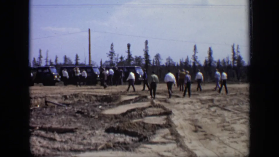 Men in suits and shirts continue toward parked vans at an outdoor Moscow field site in the 1971 home-movie footage.