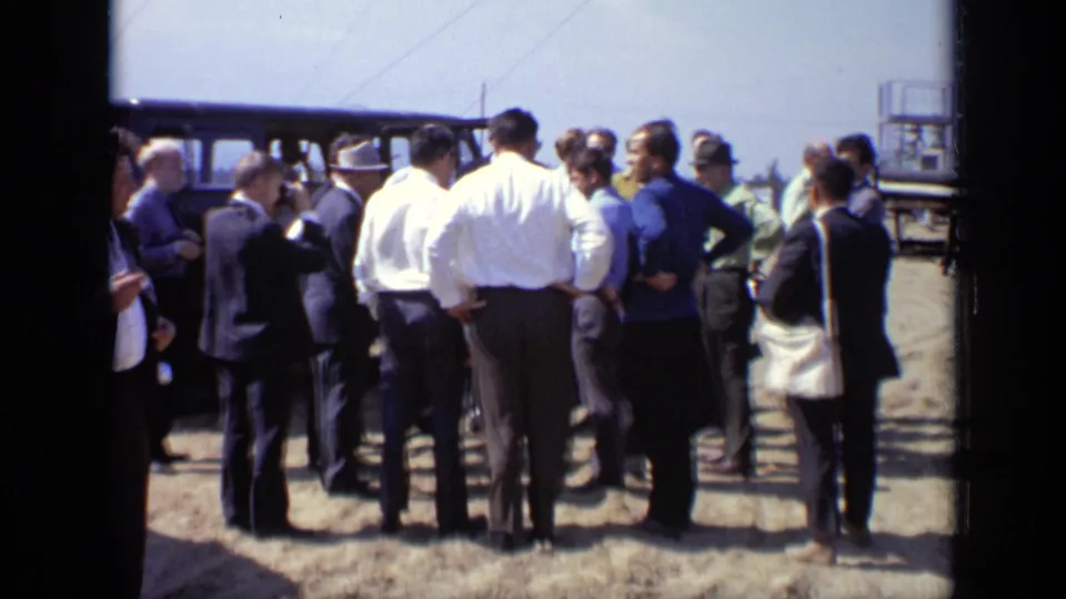 Closer 1971 Moscow view of men gathered beside a dark van, with suits, shirts, and bags visible in bright daylight.