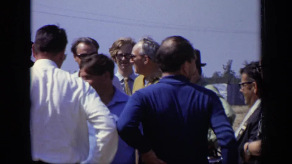 Adult men in 1971 Moscow appear to converse outdoors, including a blue-shirted man seen from behind and several men wearing glasses.