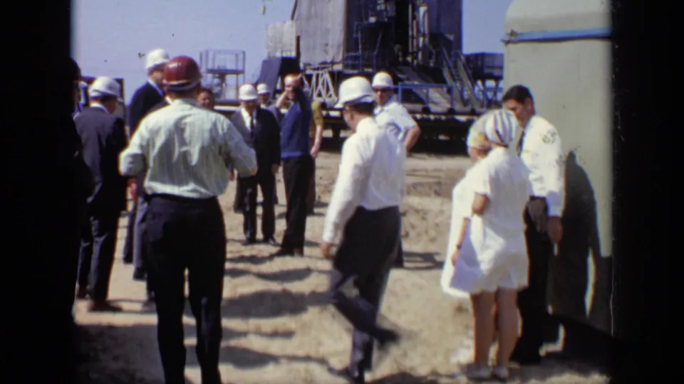 A 1971 Moscow construction-site group walks near equipment, including hard-hatted men and a woman in a light dress.