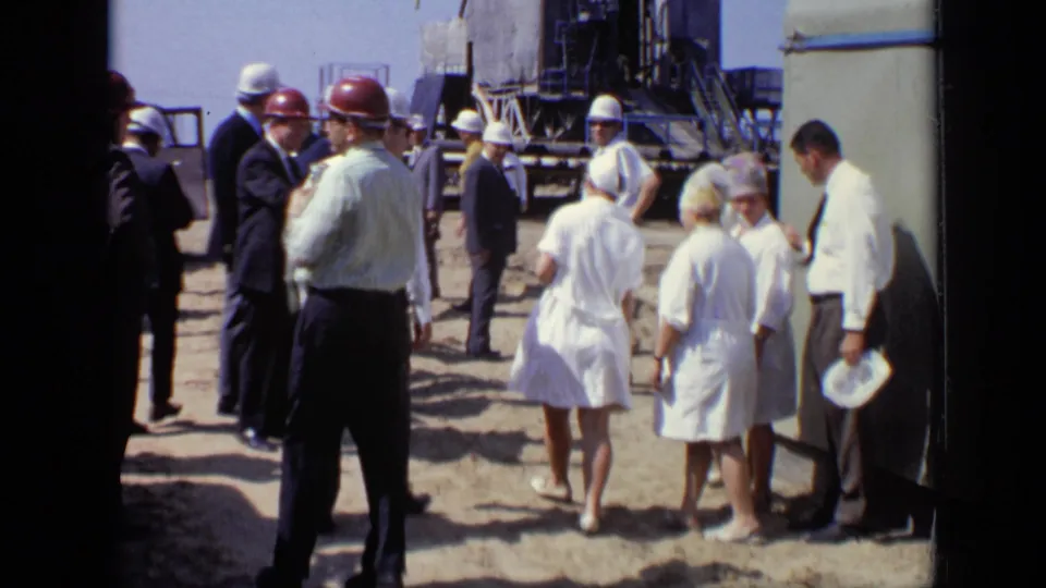 Adults at a Moscow industrial site in 1971 stand and converse beside heavy metal equipment or construction structure.