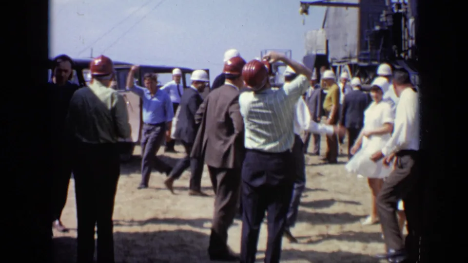 1971 Moscow frame showing a hard-hat group dispersed across a dusty industrial site, with people walking and talking.
