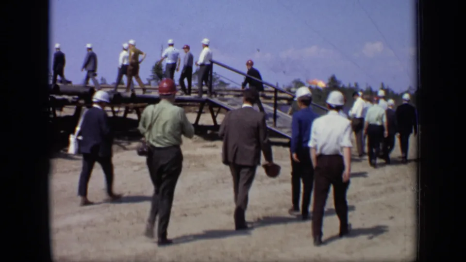 Men in hard hats and business clothing walk across a dusty Moscow worksite near pipes and equipment in 1971 8mm footage.
