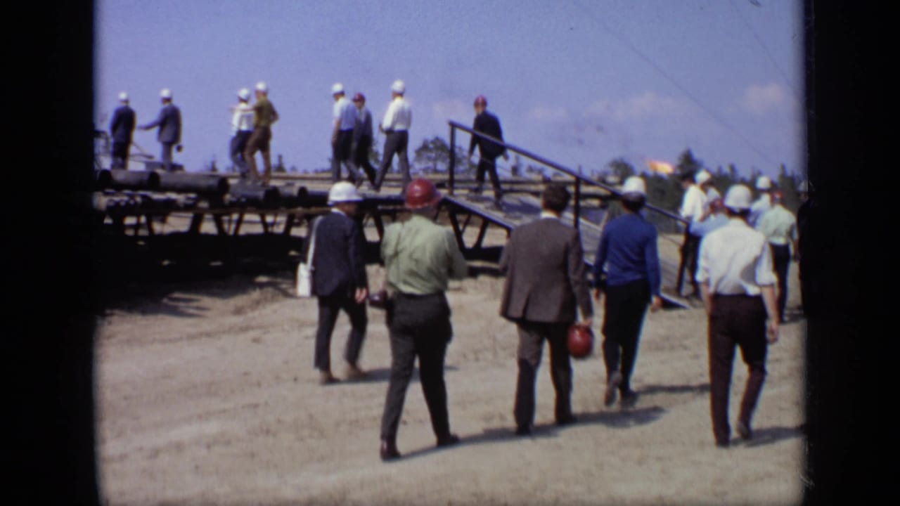 1971 Moscow footage shows men in business attire and hard hats walking toward a raised platform with pipes at an industrial site.