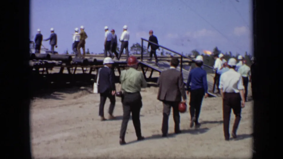 1971 Moscow footage shows men in business attire and hard hats walking toward a raised platform with pipes at an industrial site.