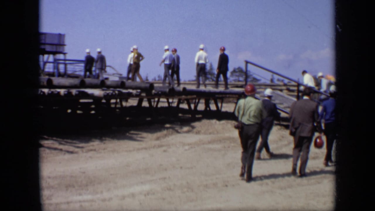 Men in hard hats and business clothing walk along a raised platform at a Moscow industrial site in 1971.