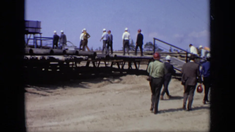 Men in hard hats and business clothing walk along a raised platform at a Moscow industrial site in 1971.