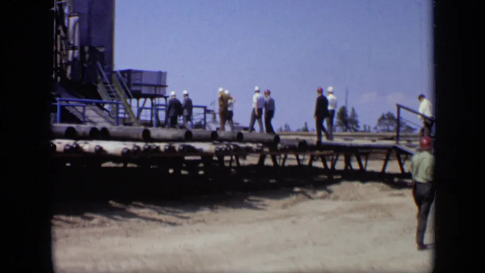 1971 Moscow industrial footage shows men in hard hats and suits walking near steps, piping, and heavy site structures.