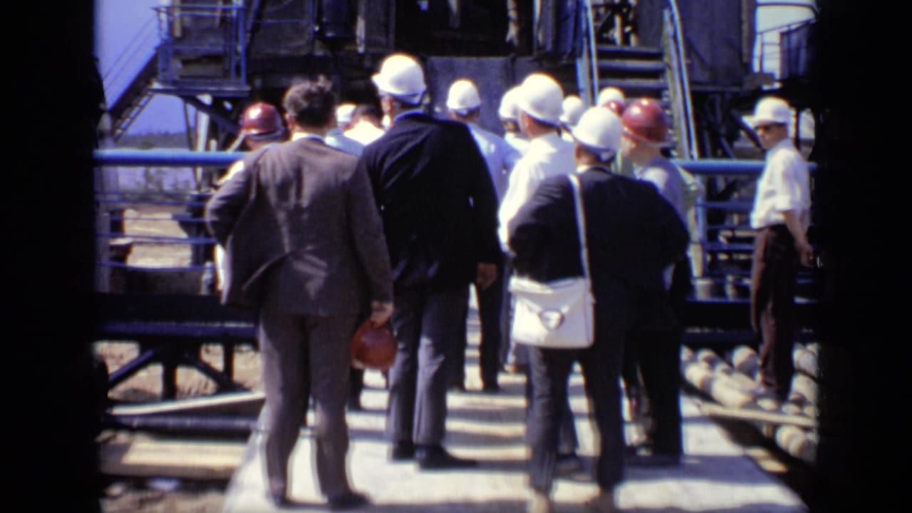 A group of suited visitors and hard-hatted personnel walk through a Moscow industrial facility on an elevated platform.