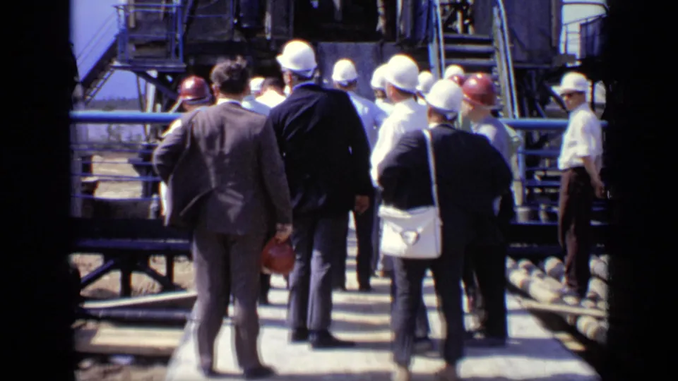 A group of suited visitors and hard-hatted personnel walk through a Moscow industrial facility on an elevated platform.