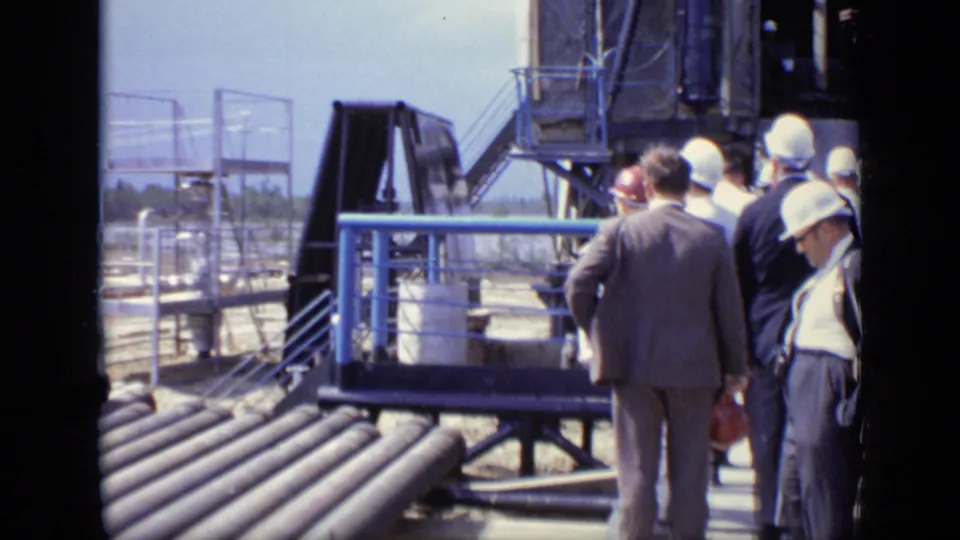 Final frame shows suited and helmeted men near blue railings, pipe runs, and heavy industrial equipment at the Moscow site.
