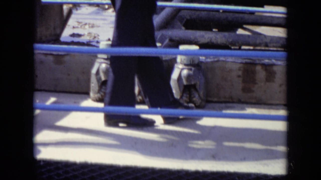 Men in trousers walk behind blue-painted railings, with metal machinery visible in this 1971 Moscow industrial scene.