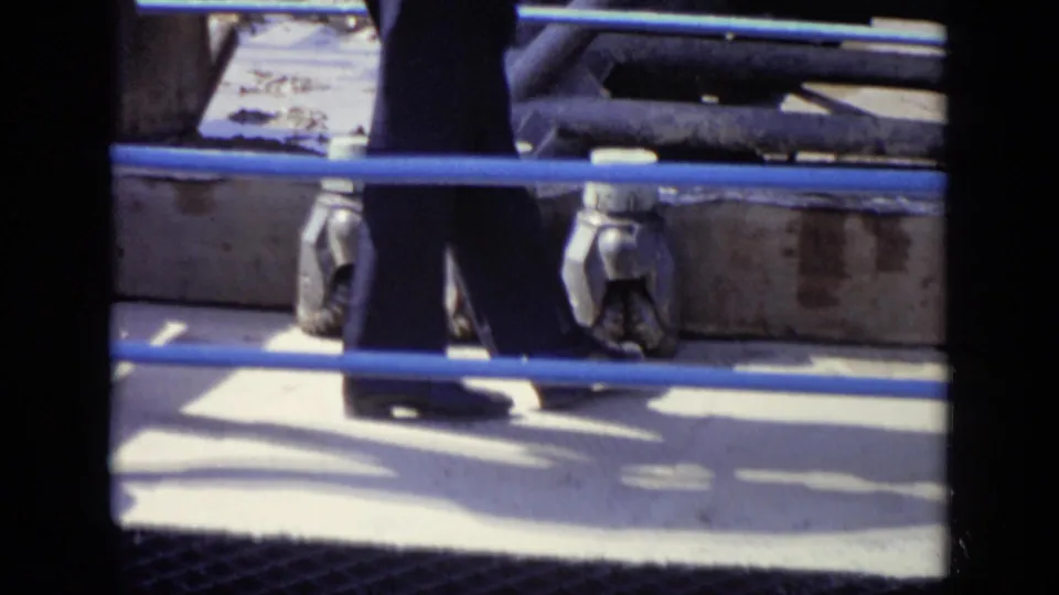 Men in trousers walk behind blue-painted railings, with metal machinery visible in this 1971 Moscow industrial scene.