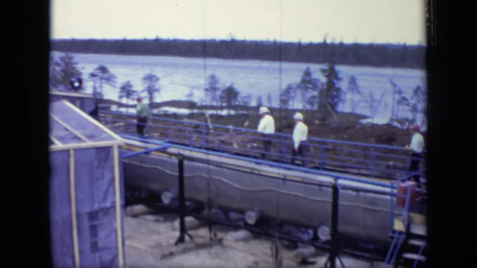 1971 Moscow riverside construction view with workers near blue railings, tanks and a broad waterway.