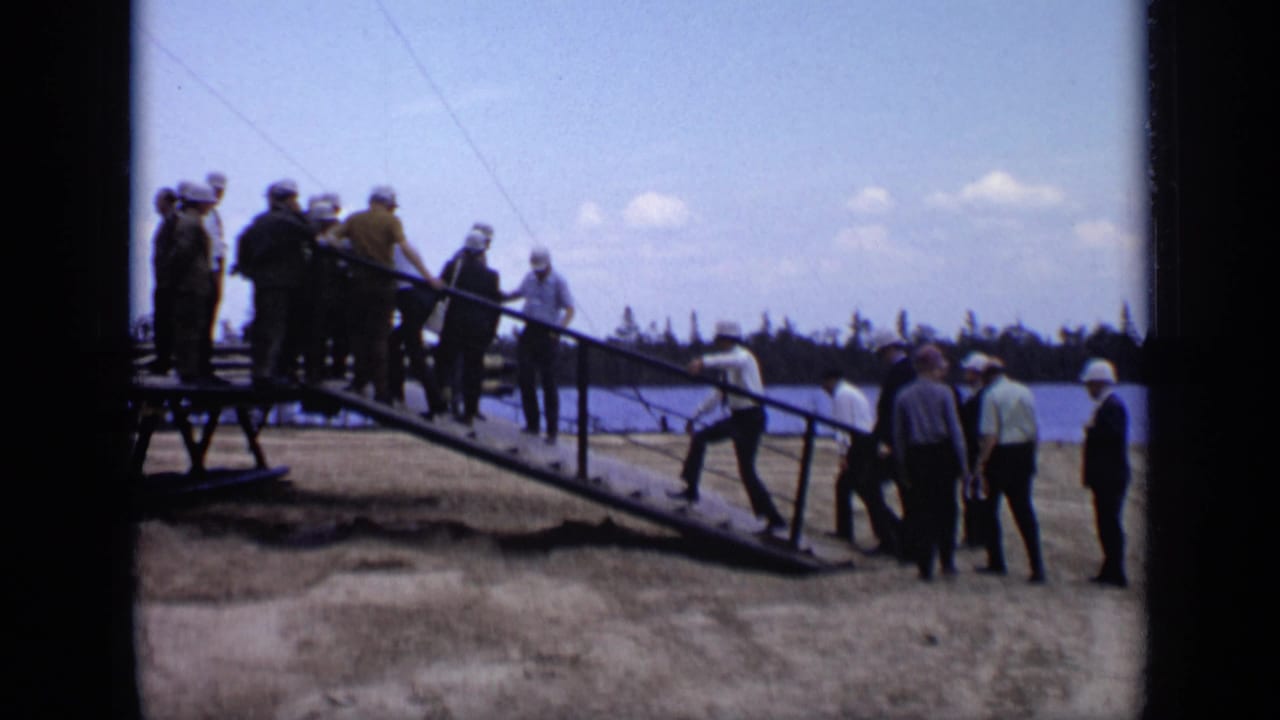 Group of men stands and walks around a sloped metal ramp outdoors.