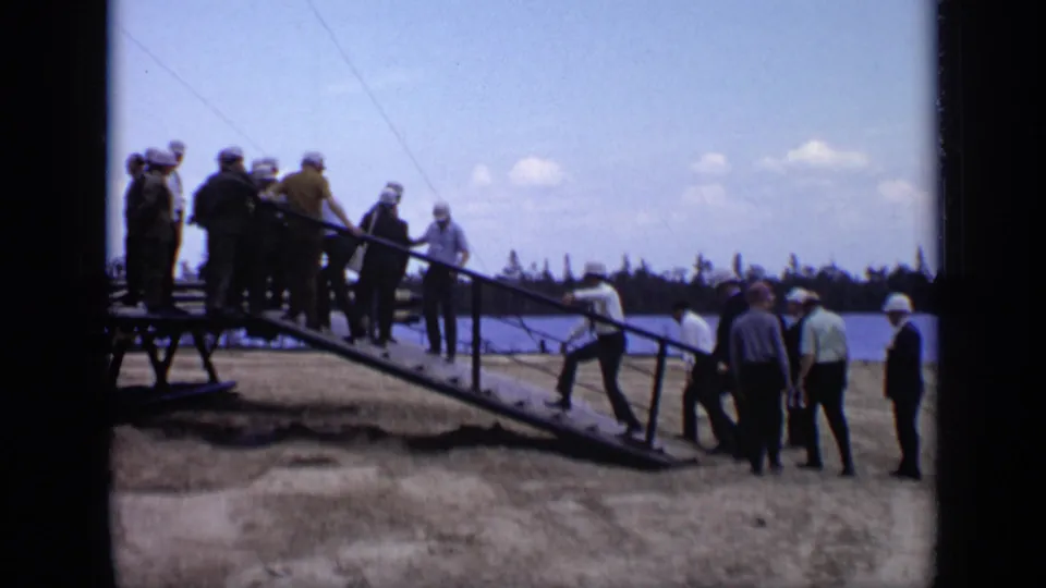 Hard-hatted workers and business-dressed visitors move around a sloped ramp at the Moscow industrial site in 1971 footage.