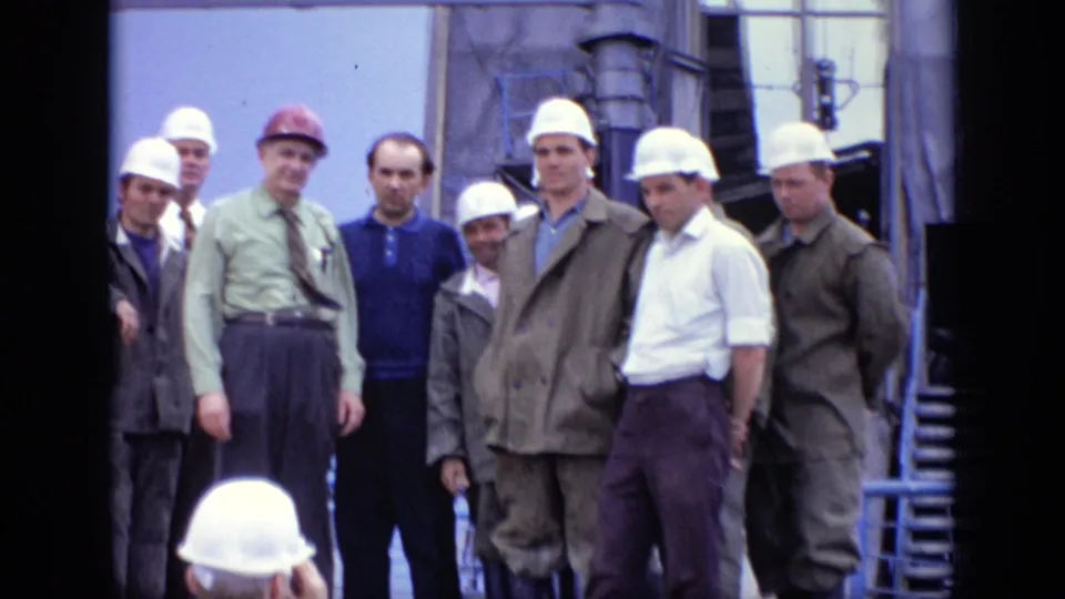A closer 1971 Moscow worksite frame shows hard-hatted men, suited officials, and workers grouped beside scaffolding and industrial equipment.