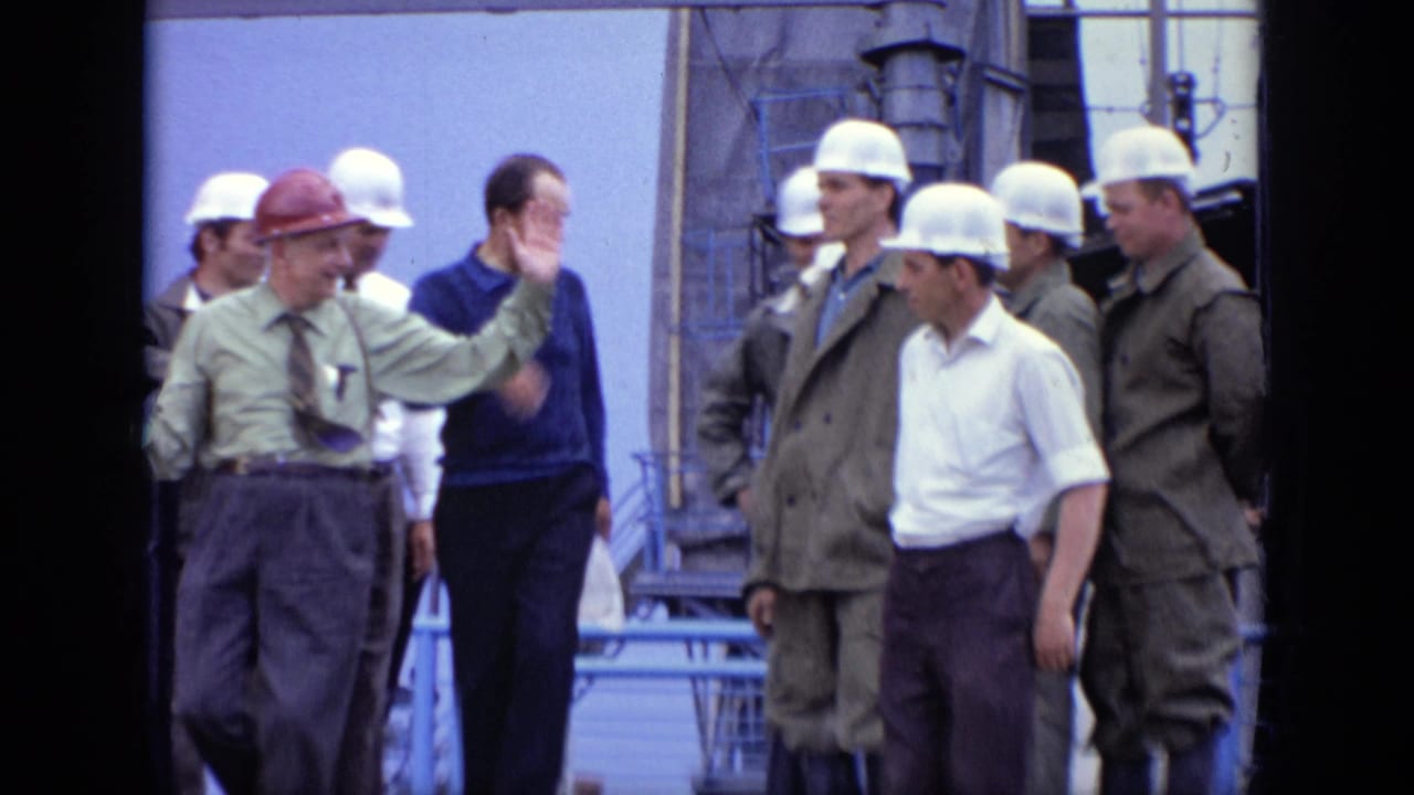 1971 Moscow frame of a supervisor in a red hard hat gesturing to workers in white hard hats at an industrial site.