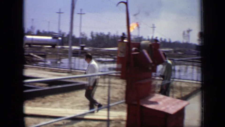 1971 Moscow industrial-site frame showing men near railings, pipework, utility poles, and a distant gas flare.