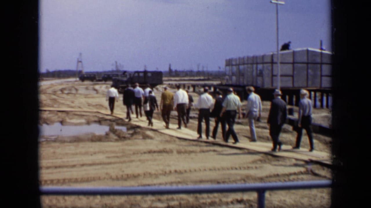 Men walking on planks across a muddy industrial construction site.