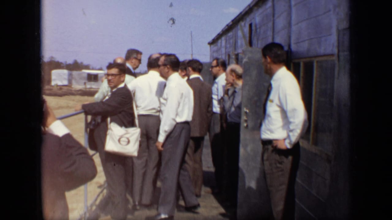 Group of men gathered by a railing beside an industrial building.