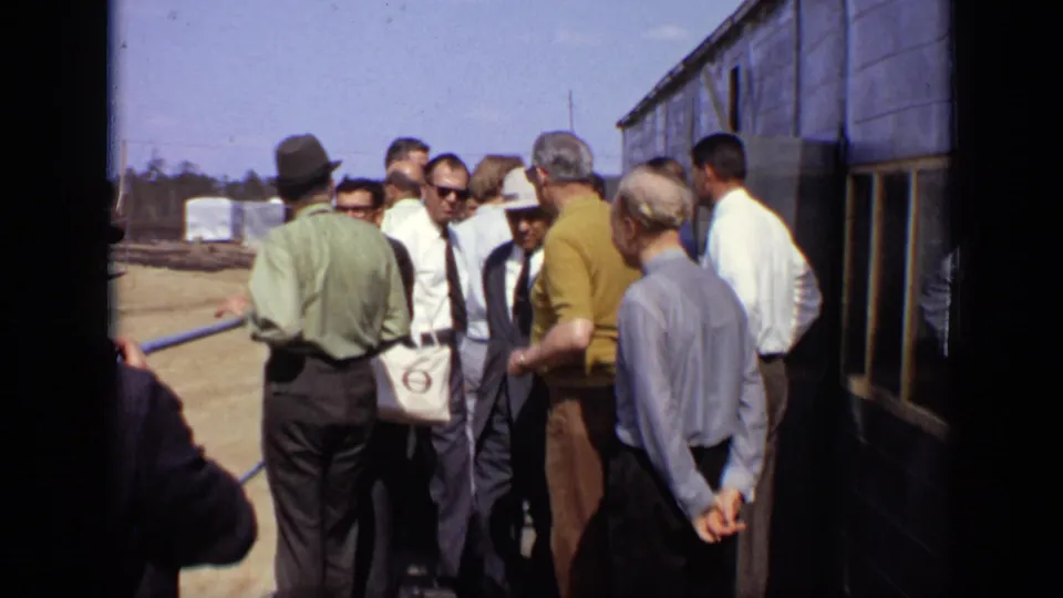 The 1971 Moscow footage shows a group of adult men clustered beside a dark building, some in suits, shirts, and sunglasses, near a railing.