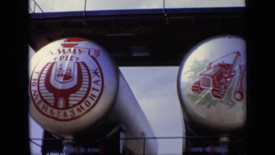 Two large industrial tanks in the Moscow sequence, one with Cyrillic branding and another painted with machinery artwork.