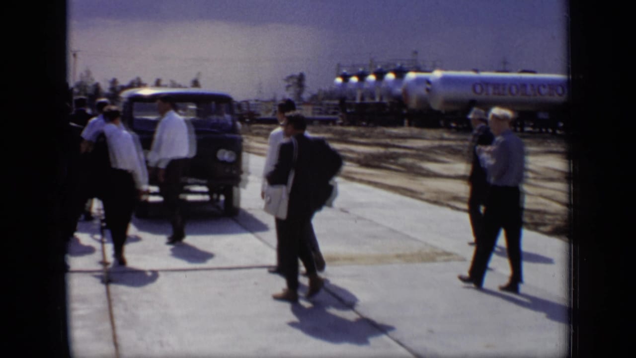 Officials at a Moscow industrial site stand near a dark van, with silver flammable tankers visible behind them.
