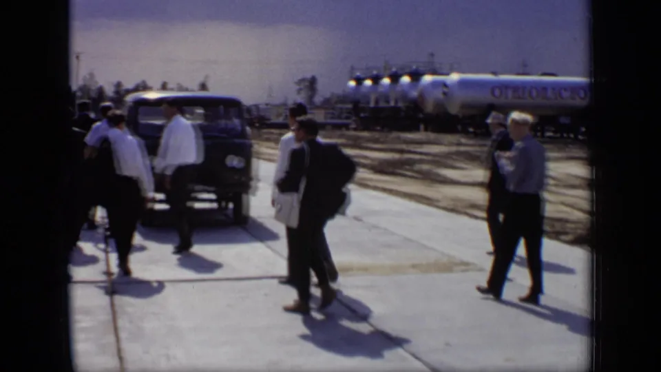 Officials at a Moscow industrial site stand near a dark van, with silver flammable tankers visible behind them.