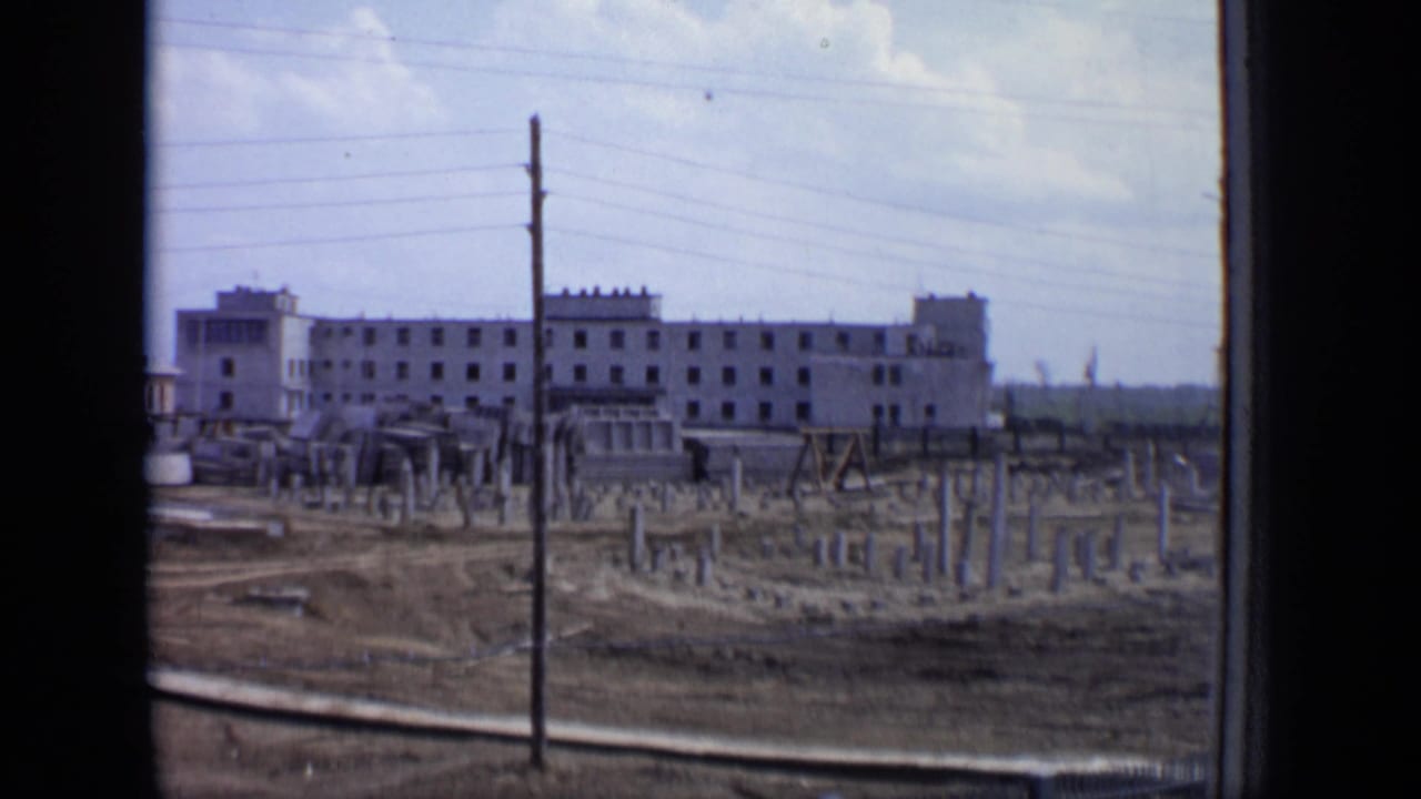 1971 Moscow train-view frame showing a large unfinished building, bare lots, utility poles, and scattered construction materials.