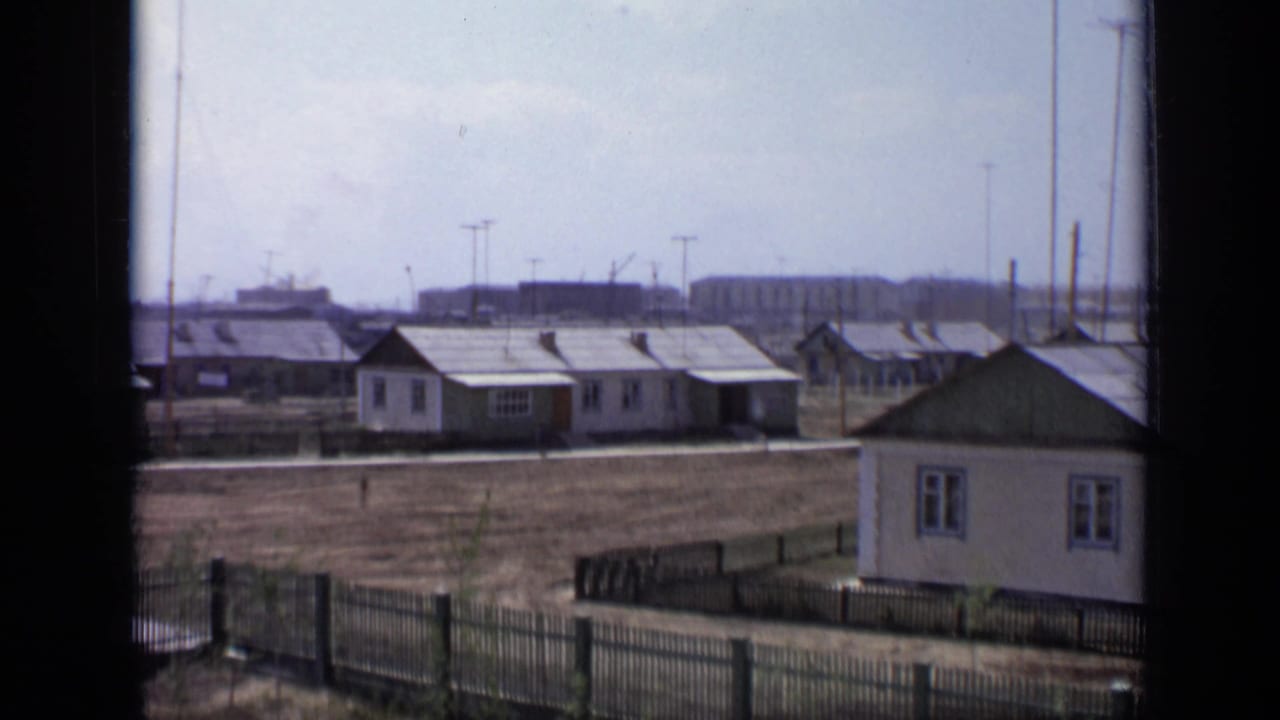 Small dwellings and fenced ground with long low buildings in the distance.