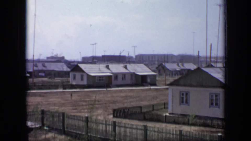 1971 Moscow exterior view of small dwellings, fences, bare open ground, rooftop antennas, and distant industrial buildings.