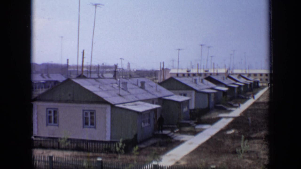 Low-rise houses beside a paved walkway with utility poles and distant buildings.