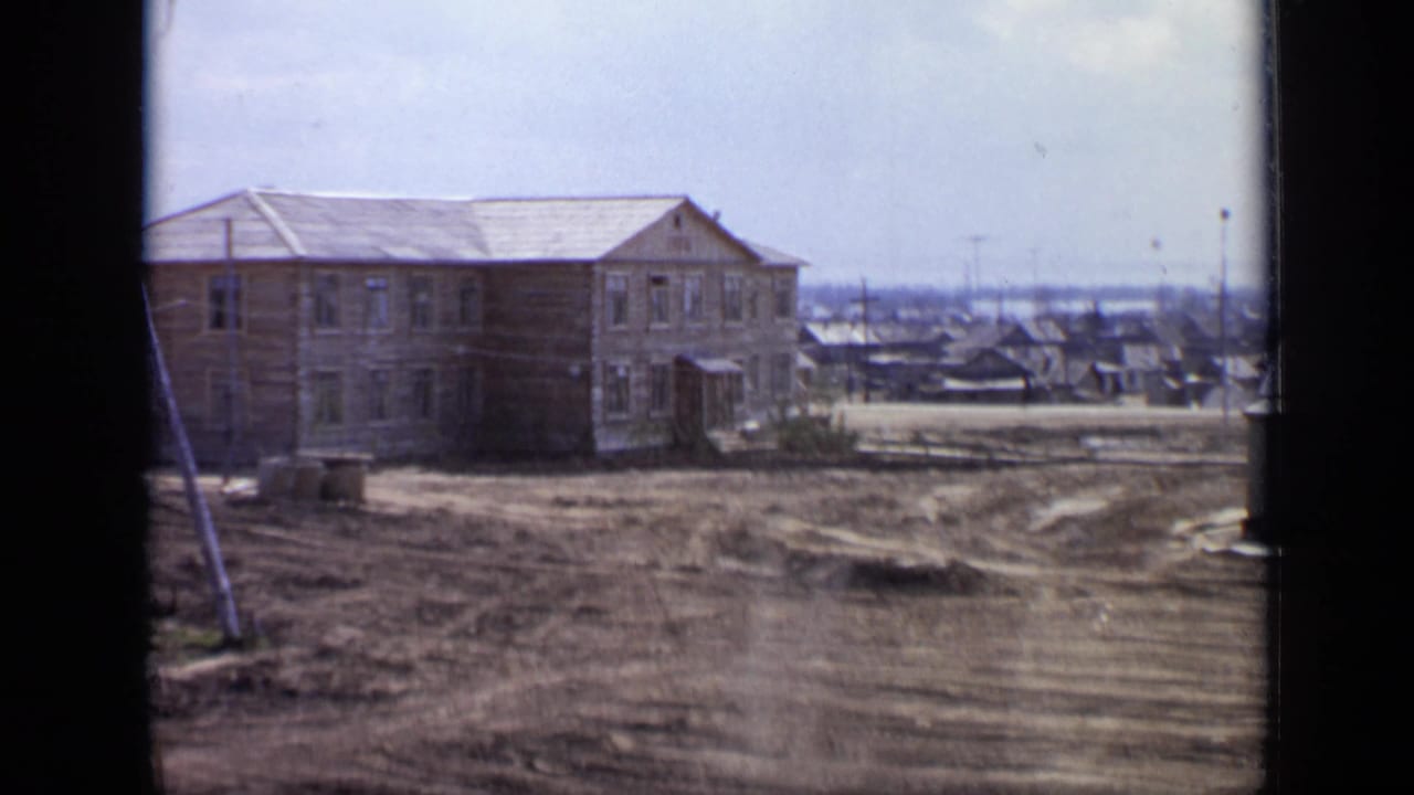 Two-story wooden building beside a dirt lot, seen through dark window-frame edges.