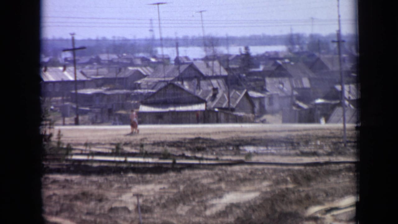 A 1971 Moscow roadside view shows a pedestrian near simple houses, utility poles and open ground on soft 8mm film.