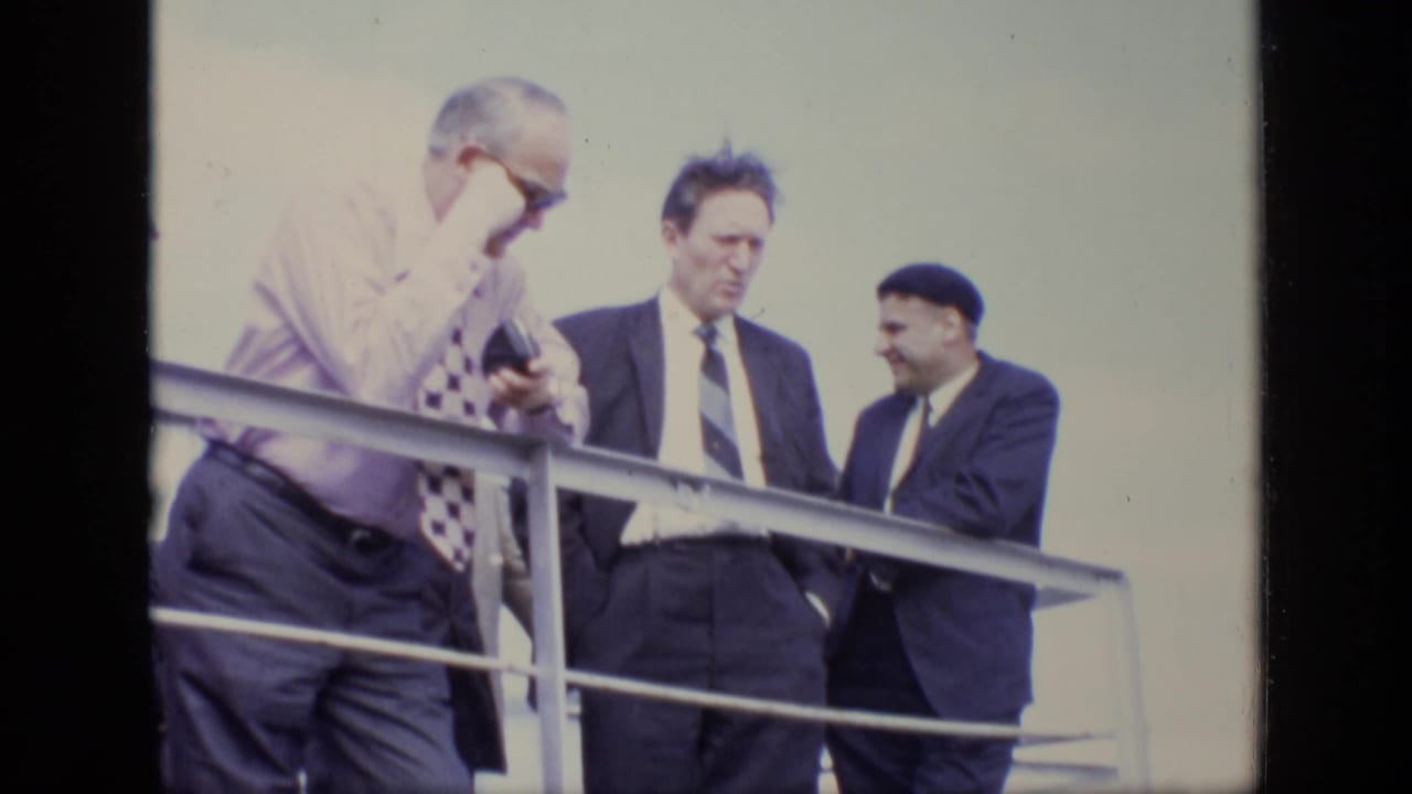 In 1971 Moscow footage, three adult men in business attire stand on a balcony or raised walkway near a metal railing.