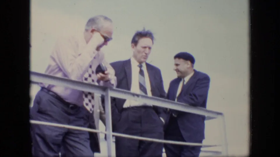 In 1971 Moscow footage, three adult men in business attire stand on a balcony or raised walkway near a metal railing.
