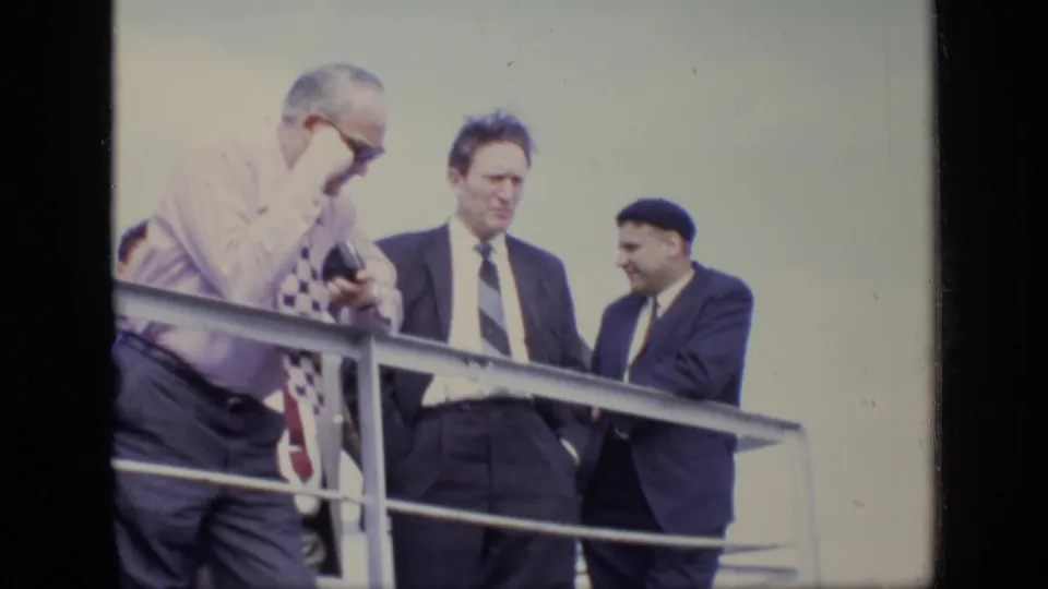 Three men in formal clothing stand near a metal railing in the 1971 Moscow clip, with soft focus and faded color.